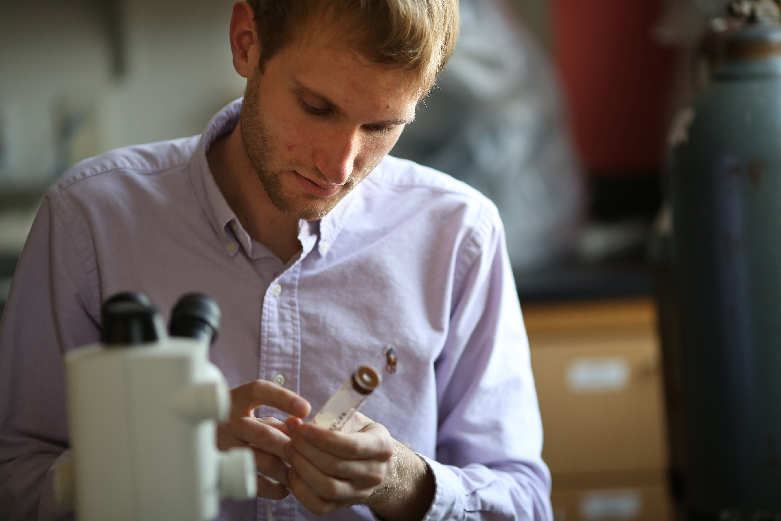 Student is examining a suringe-like object with a microscope in the foreground.