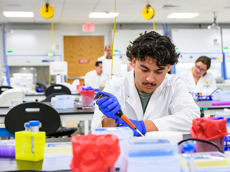 Male student uses equipment in laboratory setting with several people working in the background.