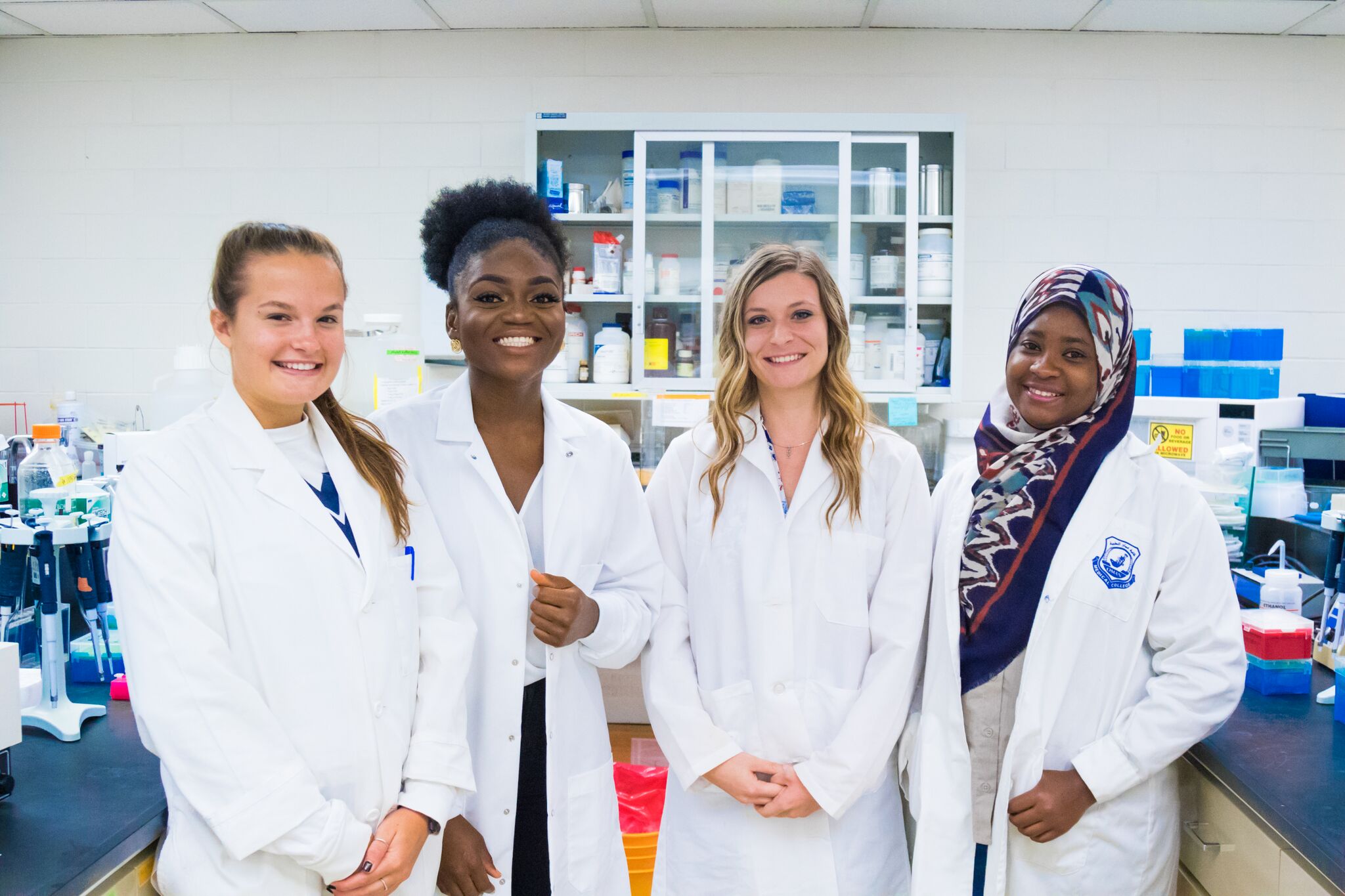 A group of four co-ed students in white coats posing for a picture in a laboratory.