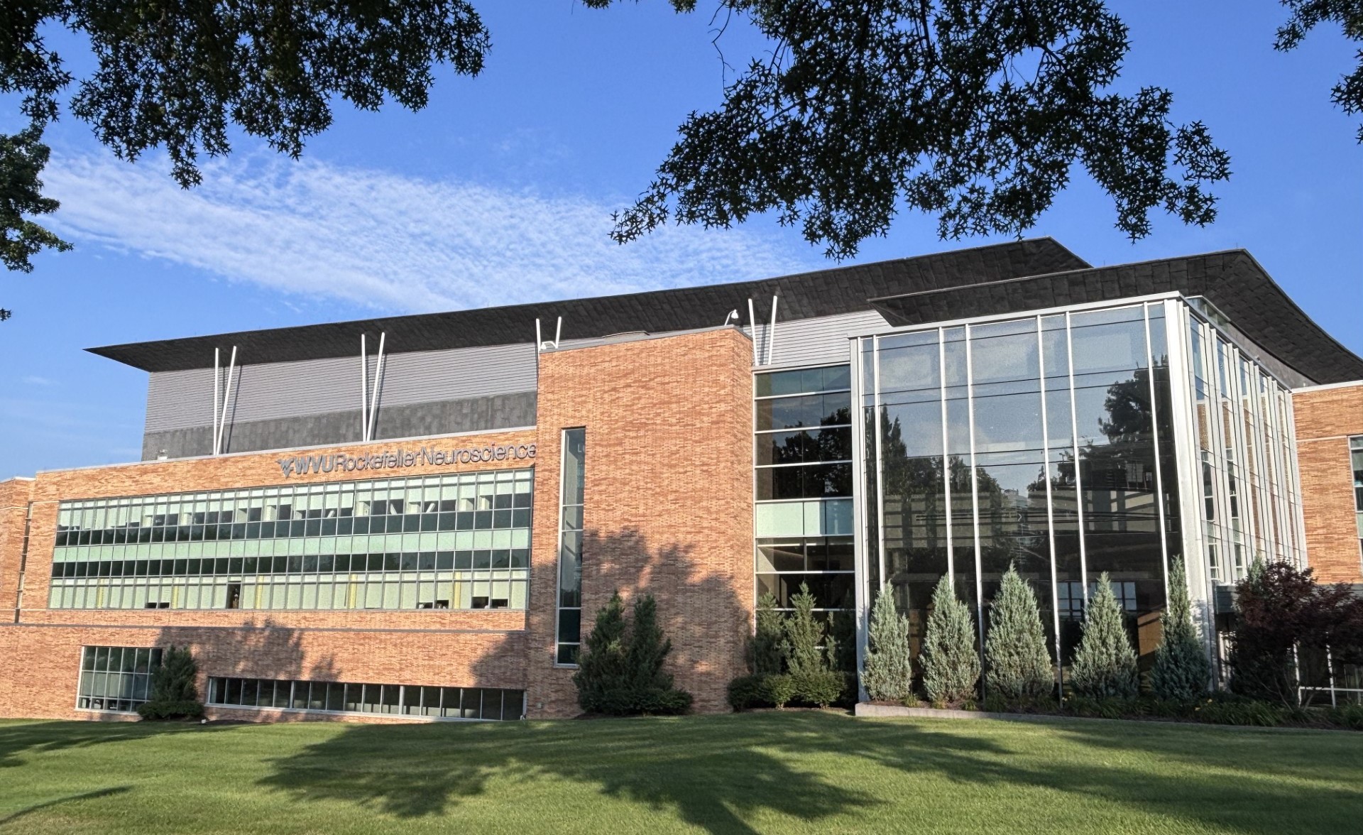 The front facade of the WVU Rockefeller Neuroscience Institute building on a summer day with clear skies.