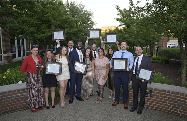Residents holding their degrees held high while standing in a common breezeway between flowers on a stone walkway.